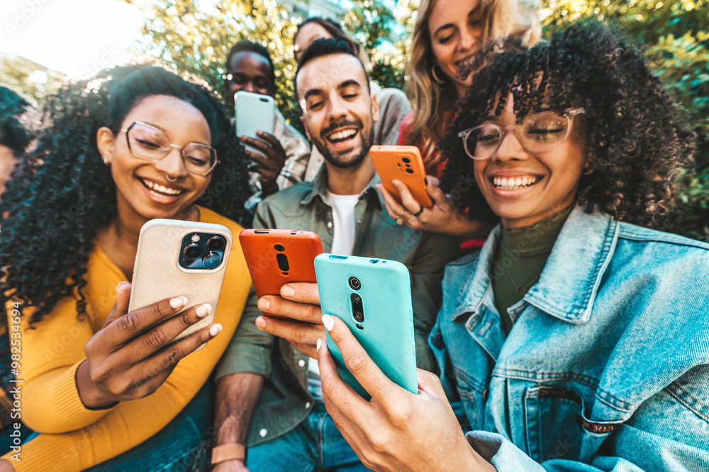 Obraz premium Group of young people using smart mobile phone outdoors - Happy friends with smartphone laughing together watching funny video on social media platform - Tech and modern life style concept