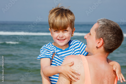 Smiling child in striped shirt hugged by adult near the ocean