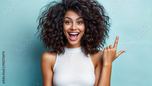 Cheerful Young Woman Smiling and Pointing with Joy Against a Soft Blue Background