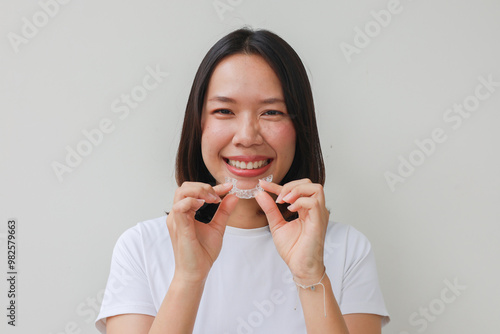 close up young asian woman smiling with hand holding dental aligner retainer (invisible) at dental clinic for beautiful teeth treatment course concept	
 photo