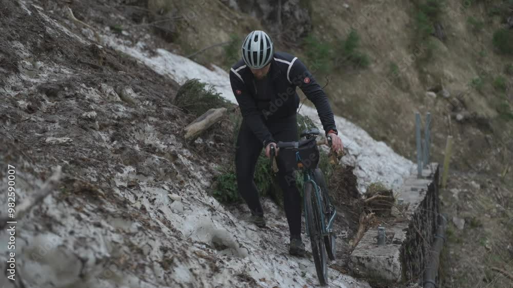 Man cyclist pulls bicycle through avalanche in mountains. Bicyclist is trapped in obstacle and is pulling his cycle through an ice slide with bicycle in his hands. Avalanche on cycling route in Alps. Man cyclist pulls bicycle through avalanche in mountains. Bicyclist is trapped in obstacle and is pulling his cycle through an ice slide with bicycle in his hands. Avalanche on cycling route in Alps.