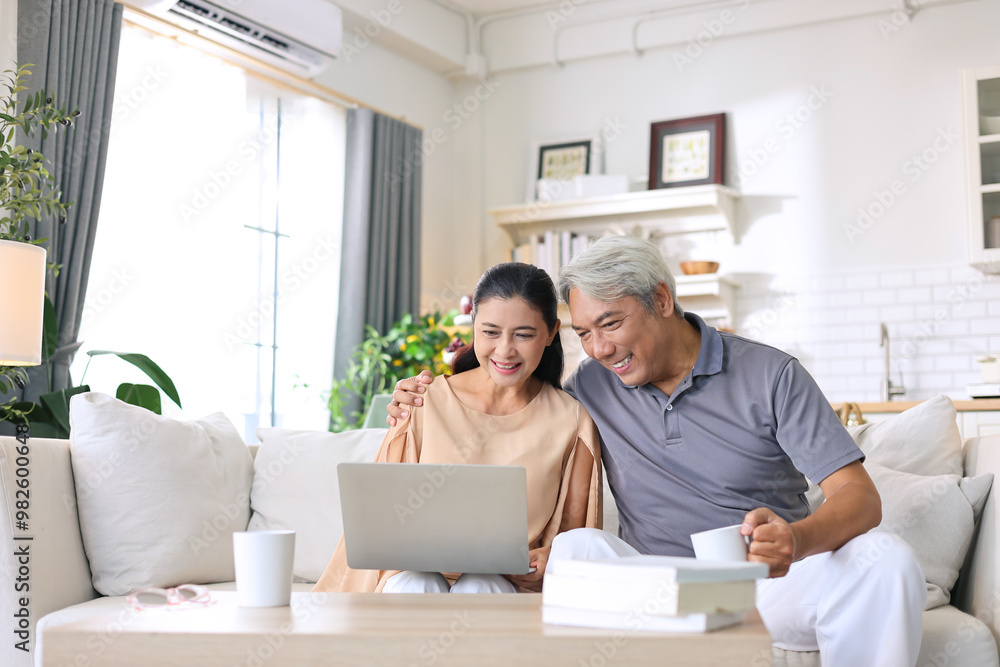 Asian senior woman happily watching movie on laptop with her elderly husband on sofa at home. Asian senior woman happily watching movie on laptop with her elderly husband on sofa at home.