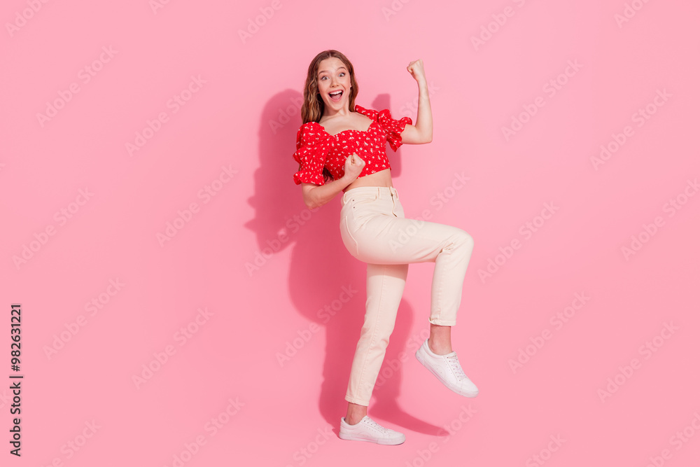 Full length photo of lovely teen lady winning raise fists dressed stylish red garment isolated on pink color background Full length photo of lovely teen lady winning raise fists dressed stylish red garment isolated on pink color background
