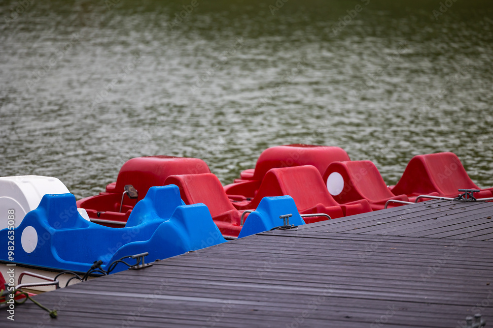 Red and blue pedalo parked on the pond next to the wooden jetty. Water recreation equipment ready for action