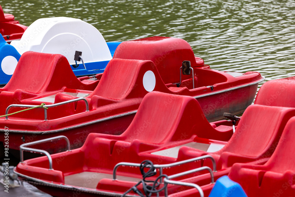 Red and blue pedalo parked on the pond next to the wooden jetty. Water recreation equipment ready for action