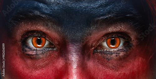 Fotografie Close-up of a woman glowing demonic eyes with face partially painted in red and black