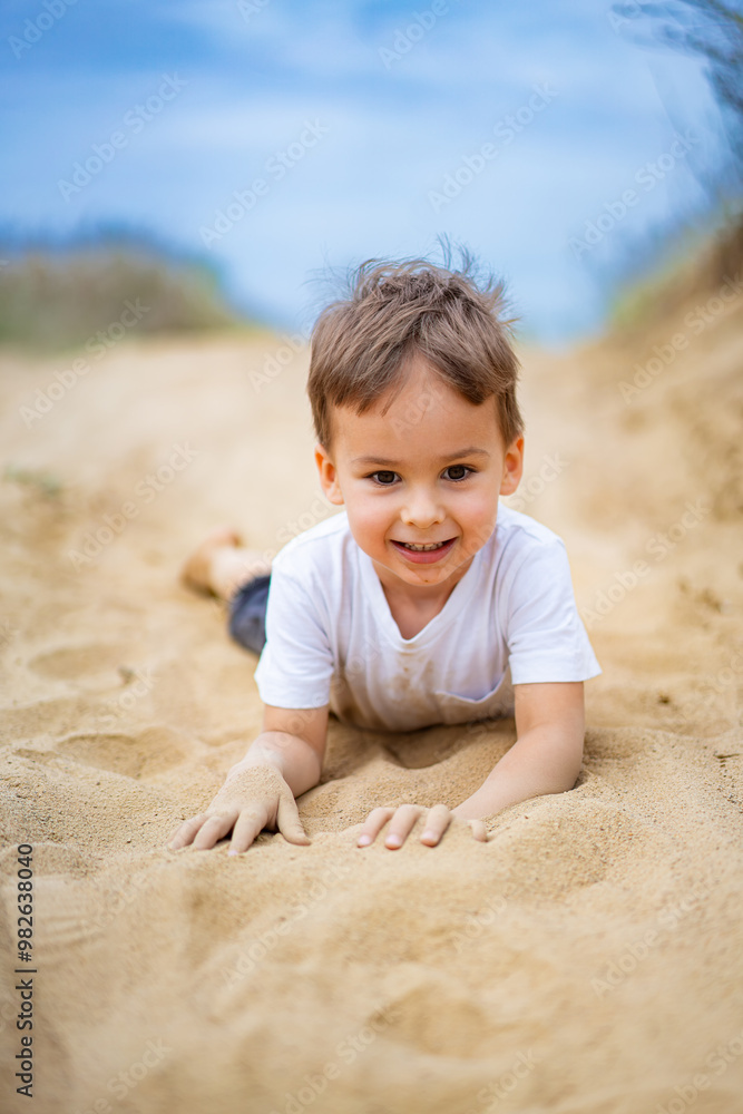 Child playing joyfully in sandy beach setting during daytime. A young boy enjoys crawling through soft sand at the beach, smiling broadly and basking Child playing joyfully in sandy beach setting during daytime. A young boy enjoys crawling through soft sand at the beach, smiling broadly and basking