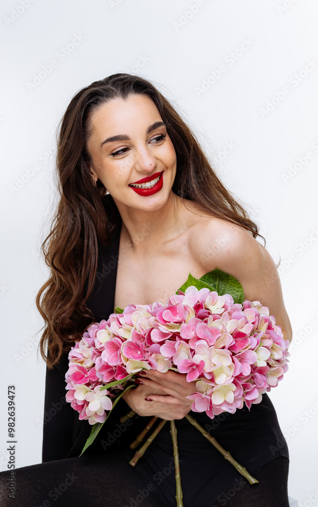 Young woman with pink flowers posing in bright studio light. A young woman smiles while holding a bouquet of pink flowers Young woman with pink flowers posing in bright studio light. A young woman smiles while holding a bouquet of pink flowers