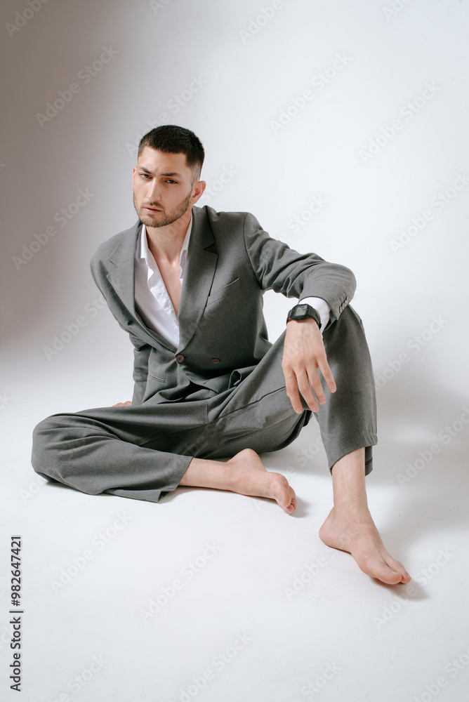 Handsome man in grey suit sits on the floor barefoot Handsome man in grey suit sits on the floor barefoot