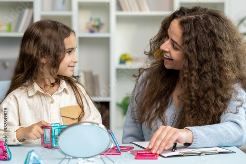 Cute long-haired girl exercising with a mirror at the speech therapist office