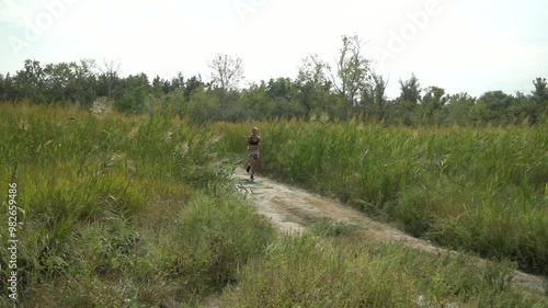 Adult woman is cardio sport and running on reed meadow. Health jogging of fitness girl is training outdoor. Concept of workouts running and healthy lifestyle. Track path of athletic young adult.