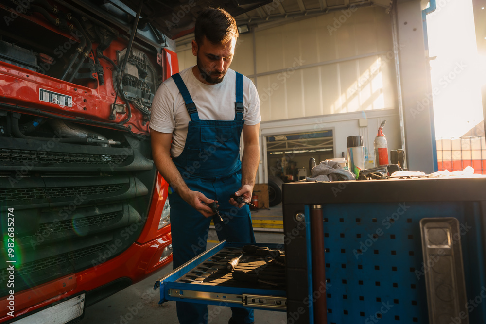 Repair man working on a vehicle in a garage. He is pulling out a drawer from a tool chest filled with tools, with sunlight streaming in from the side. Repair man working on a vehicle in a garage. He is pulling out a drawer from a tool chest filled with tools, with sunlight streaming in from the side.