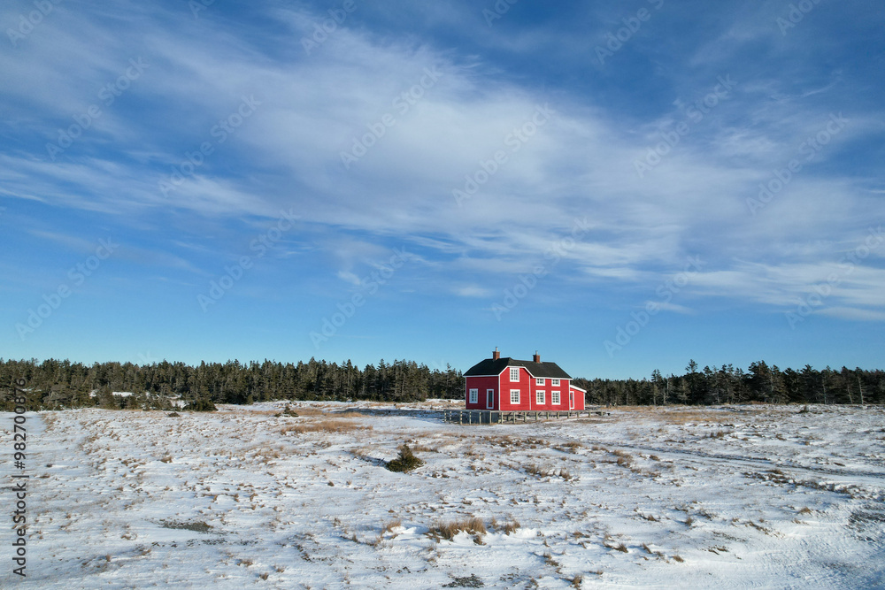 Ancient Refurbished Large Red Canadian House in Sainte-Claire Bay, in the Middle of a Frozen Snow Meadow during Winter. The old village from the 18th century is visible from above.