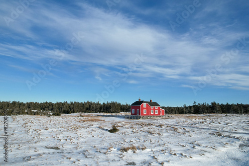 Obraz na płótnie Ancient Refurbished Large Red Canadian House in Sainte-Claire Bay, in the Middle of a Frozen Snow Meadow during Winter. The old village from the 18th century is visible from above. w salonie