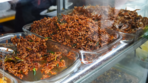 Food stalls called warteg share a variety of buffet traditional menus of indonesia with vegetables, chicken curry sauce, beef, eggs, tofu, tempeh. Menu in glass display case.  photo