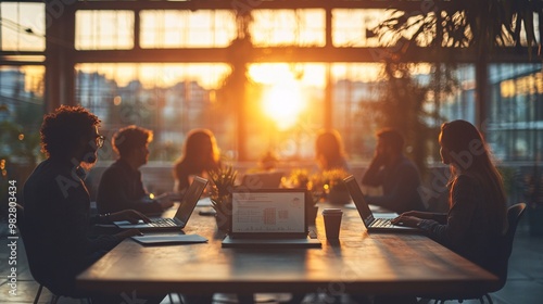 A multicultural group of employees brainstorming ideas, using laptops and a digital whiteboard in a well-lit office. The image is shot from a distant corner, partially obscured by a blurry object.
