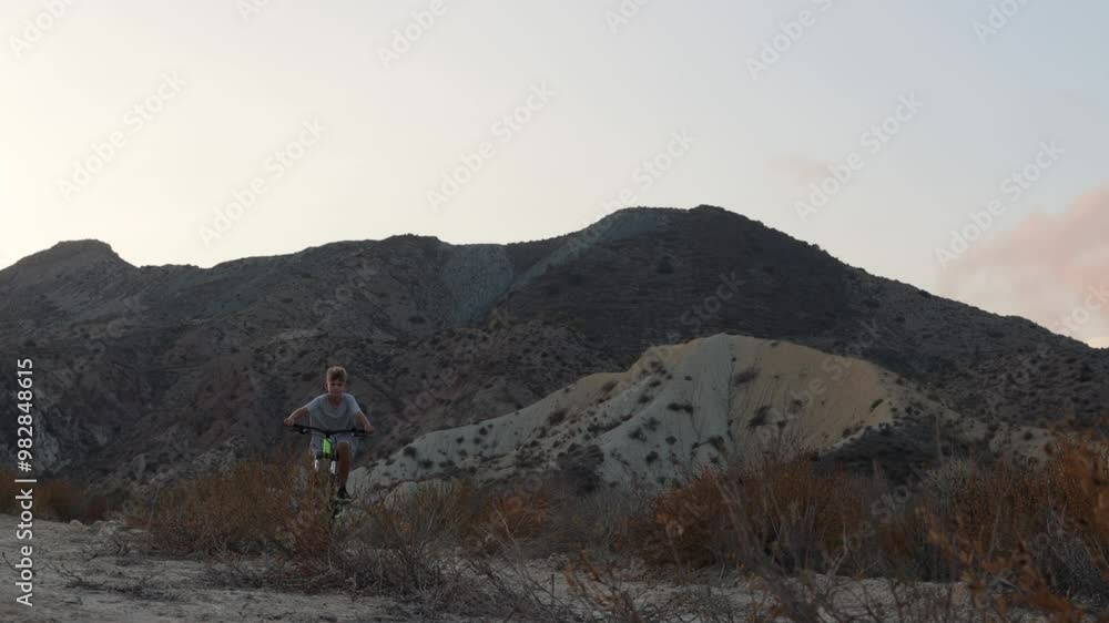 Young boy rides bike through desert, smiling and relishing journey. stunning sunset bathes scene in warm golden hour light Young boy rides bike through desert, smiling and relishing journey. stunning sunset bathes scene in warm golden hour light