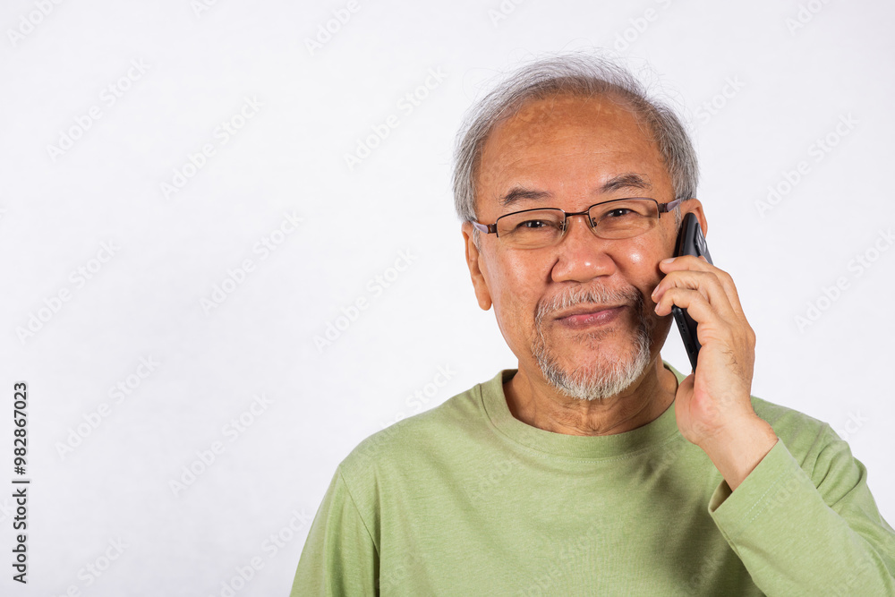 Portrait Asian smiling old man with glasses while talking on his cell phone studio shot isolated on white background, happy senior man calling to someone with mobile phone Portrait Asian smiling old man with glasses while talking on his cell phone studio shot isolated on white background, happy senior man calling to someone with mobile phone