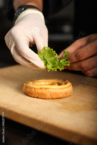 Stop motion of assembling burger. burber bon a chopping wood with Lettuce on it.  photo