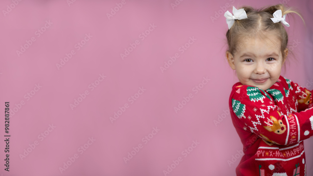 Cute baby girl beams with joy in festive red sweater with deer and Christmas trees. Child radiates joyful festive spirit of new year on bright pink background. New year, christmas, children. Cute baby girl beams with joy in festive red sweater with deer and Christmas trees. Child radiates joyful festive spirit of new year on bright pink background. New year, christmas, children.