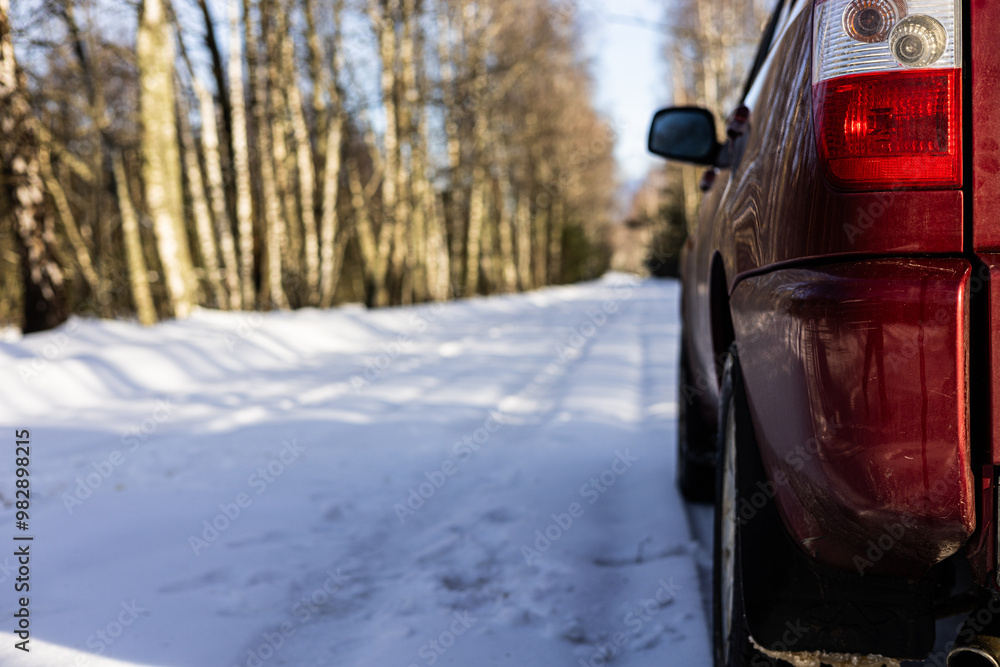 Φωτογραφία A red car is parked on the snowy side of the road that winds through the forest, and the sun casts long shadows on the snow