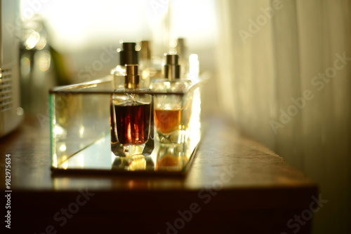 perfume bottles on a glass tray, seen on a wooden dresser by a window filled with sunlight
