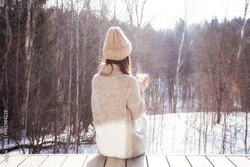 Pensive woman looking on winter forest sitting alone drinking hot tea in cold sunny winter day outdoors as loneliness concept