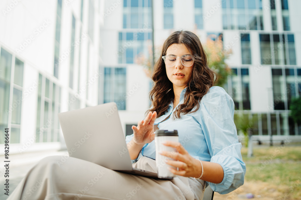 Young businesswoman is working on laptop in front of modern building Young businesswoman is working on laptop in front of modern building