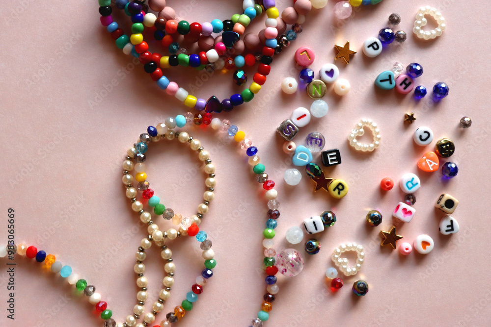 Colorful DIY necklaces, friendship bracelets and various plastic beads on pastel pink background. Flat lay.