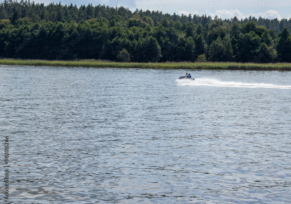A speedboat gliding across a serene lake surrounded by lush green forests, capturing the thrill of summer adventures on water. A speedboat gliding across a serene lake surrounded by lush green forests, capturing the thrill of summer adventures on water.