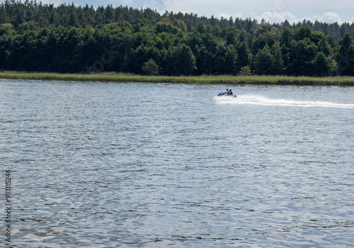 A speedboat gliding across a serene lake surrounded by lush green forests, capturing the thrill of summer adventures on water.