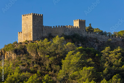 CastView of Sesimbra castle from the valley with a blue sky. The valley is covered with trees and plants. Portugal