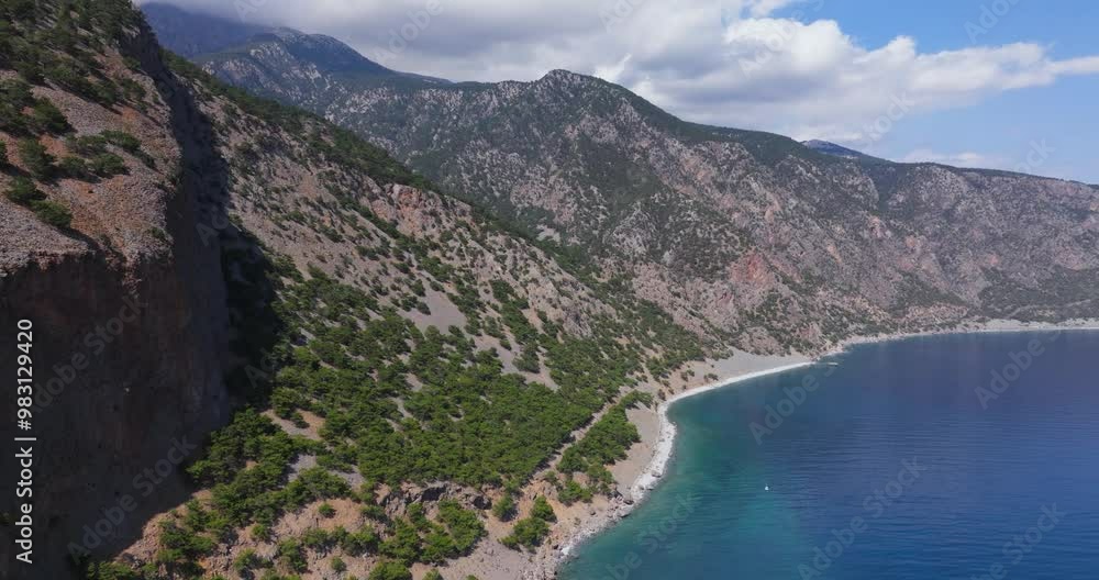 A stunning aerial view of a secluded coastal landscape with rugged mountains and a pristine beach meeting the calm, blue sea. The clear sky and vibrant greenery enhance the natural beauty of this remo A stunning aerial view of a secluded coastal landscape with rugged mountains and a pristine beach meeting the calm, blue sea. The clear sky and vibrant greenery enhance the natural beauty of this remo