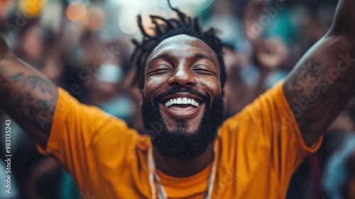 A bearded man with tattoos is ecstatically smiling with arms raised amidst a crowd, exuding exuberance and happiness in a lively, colorful celebration setting. photo