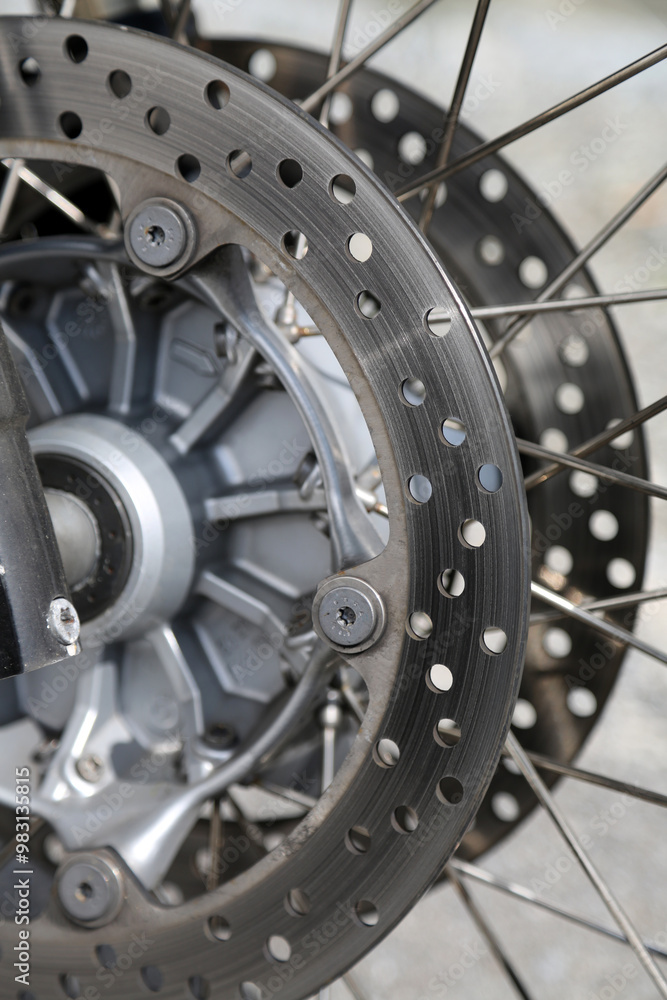 Intricate close-up of a motorcycle's wheel, showcasing its detailed brake disc and spokes against a blurred background on a serene day Intricate close-up of a motorcycle's wheel, showcasing its detailed brake disc and spokes against a blurred background on a serene day