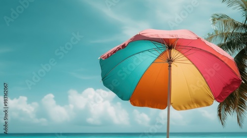 A vibrant colorful beach umbrella stands tall with an ocean and palm tree backdrop, evoking a sense of relaxation and vacation bliss. Perfect for summer and beach lovers.