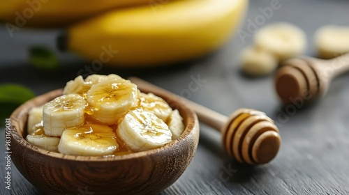 This image depicts sliced bananas drizzled with honey in a wooden bowl, with whole bananas and a honey dipper in the background, ideal for culinary and healthy lifestyle themes. photo