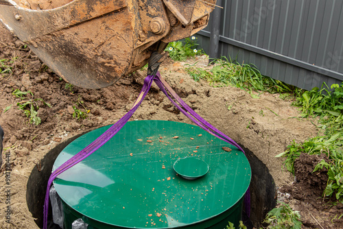 Installing septic tank in a country house. Autonomous sewerage system. Excavator lowers the septic tank into the pit
