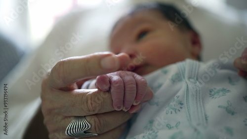 Newborn gently holding grandmother’s finger, highlighting a tender moment of connection, security, and warmth, symbolizing the bond and trust between the youngest and oldest generations photo