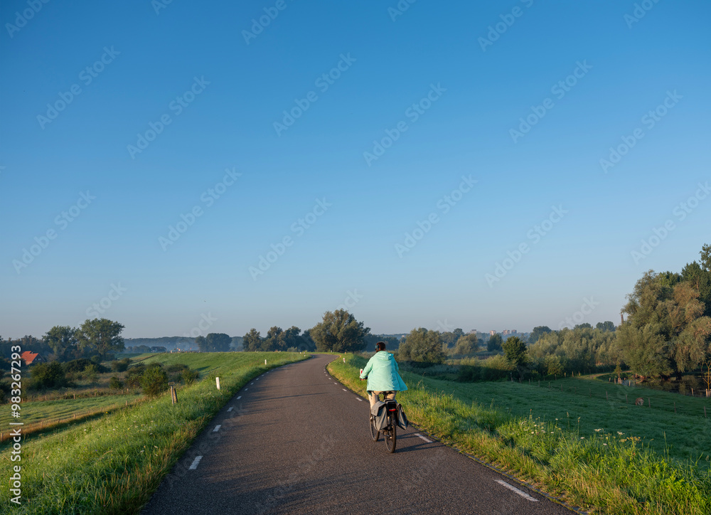 woman rides bike on dike at ooijpolder near nijmegen in the netherlands