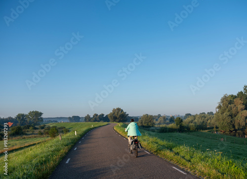 Obraz na płótnie woman rides bike on dike at ooijpolder near nijmegen in the netherlands w salonie
