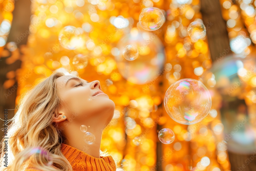 Fototapeta premium A woman with long hair smiles as she stands amid golden autumn foliage, surrounded by floating soap bubbles, capturing the essence of a peaceful fall afternoon.
