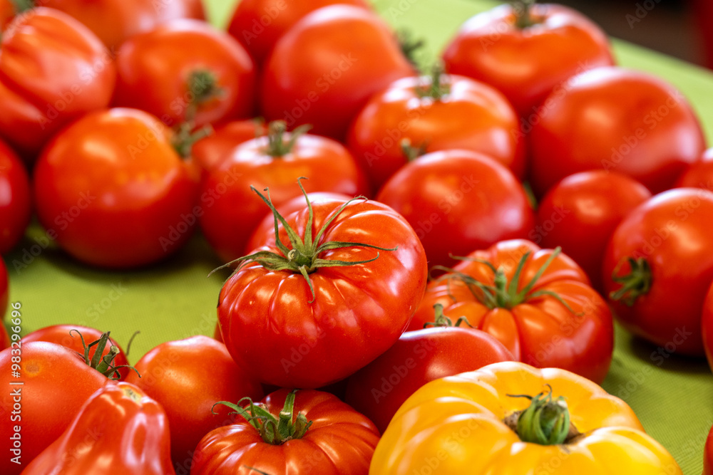 A display of various fresh tomatoes harvested for sale at a grocery. The produce is vibrant yellow, red, and orange in color with firm and shiny skin. The ripe crops are of various sizes and shapes. A display of various fresh tomatoes harvested for sale at a grocery. The produce is vibrant yellow, red, and orange in color with firm and shiny skin. The ripe crops are of various sizes and shapes.