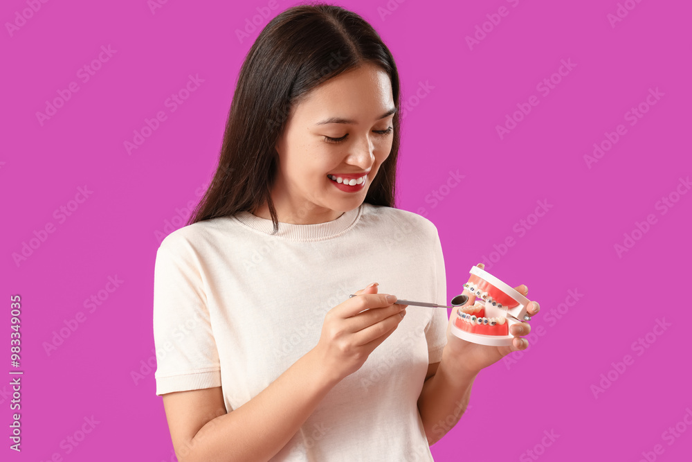 Smiling young Asian woman with jaw model and dental tool on purple background Smiling young Asian woman with jaw model and dental tool on purple background