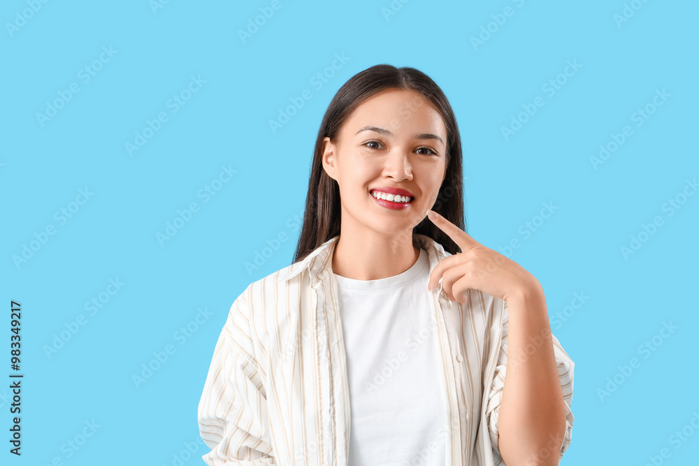 Young Asian woman pointing at her smile on blue background Young Asian woman pointing at her smile on blue background