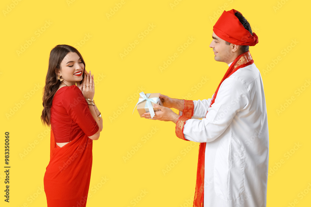 Beautiful Indian couple with gift box on yellow background Beautiful Indian couple with gift box on yellow background