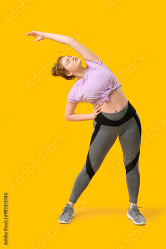 Sporty young woman doing side bend on yellow background