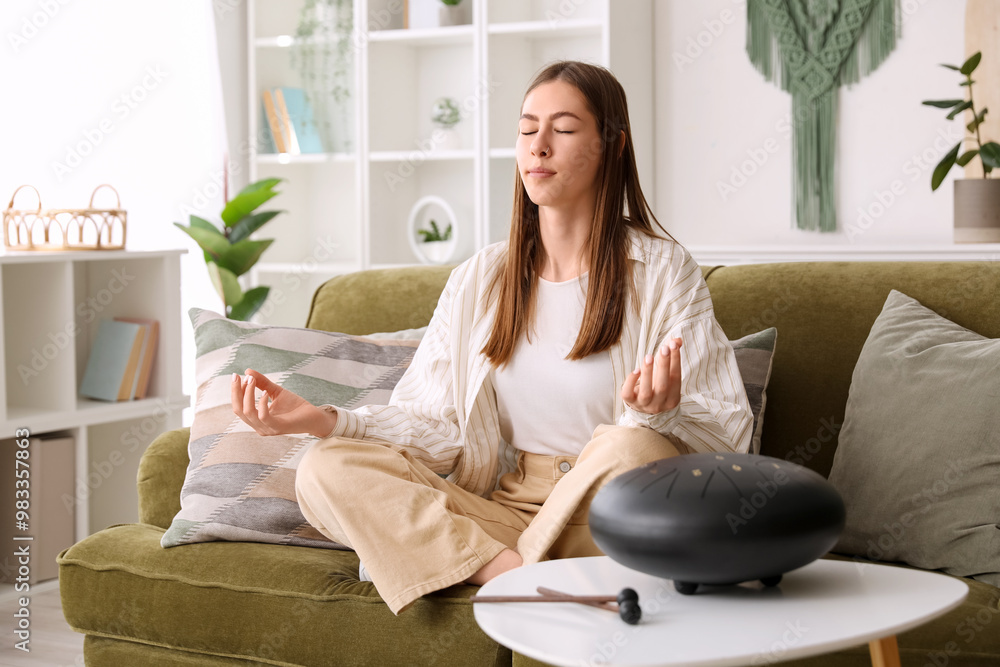 Obraz premium Young woman meditating on sofa with glucophone at home