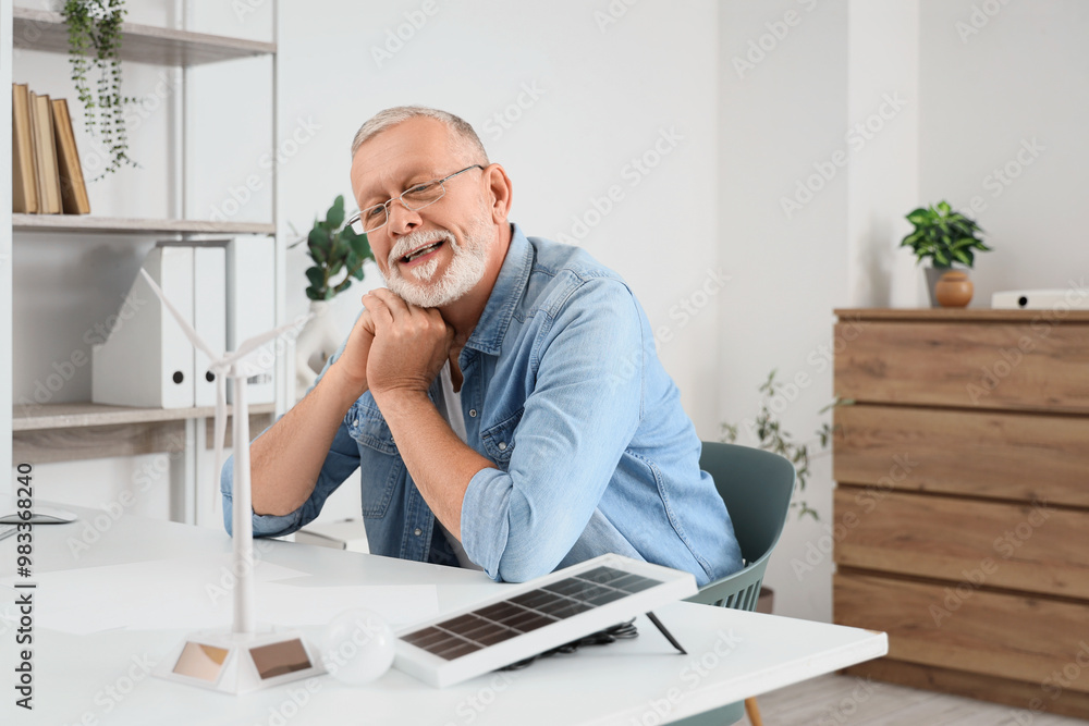 Mature engineer with wind turbine model on table in office Mature engineer with wind turbine model on table in office
