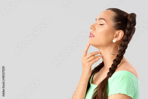 Beautiful young woman with braids on grey background